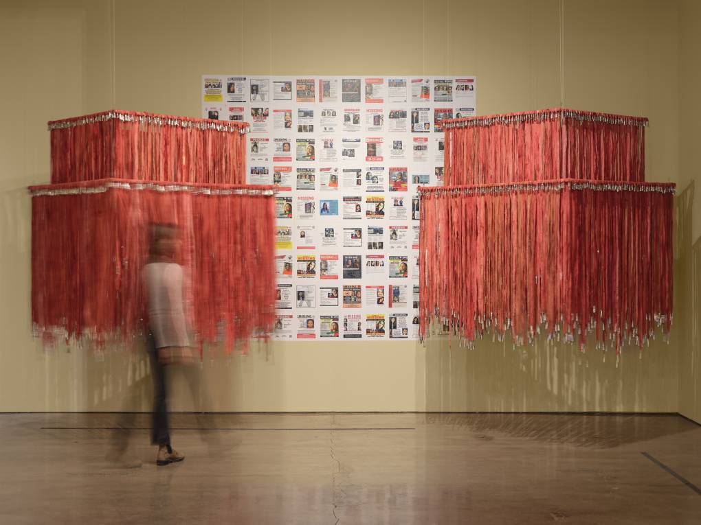 hanging red sculptures with posters on wall behind, blurry figure walking by