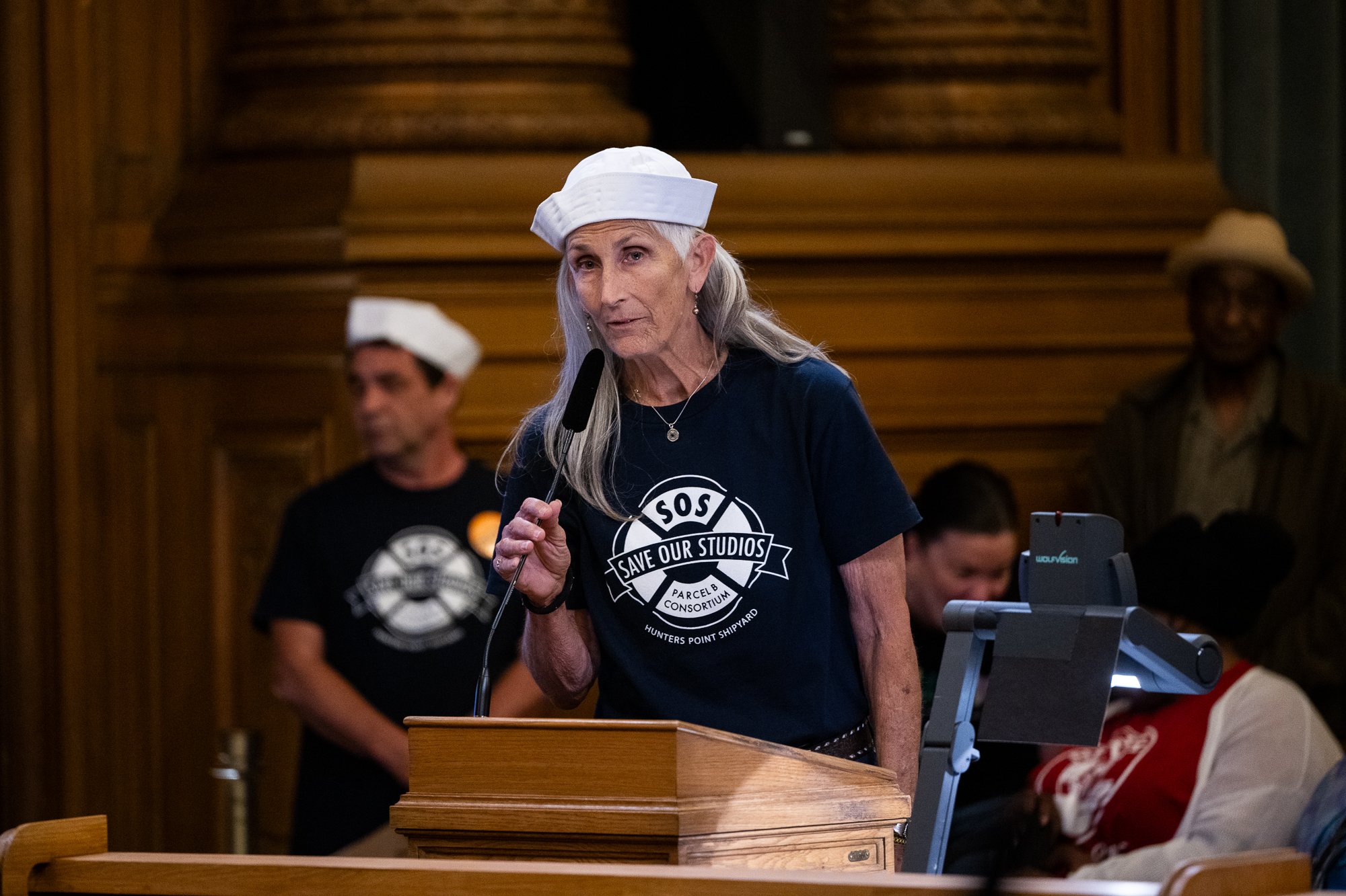 older person in white sailor hat speaks into mic