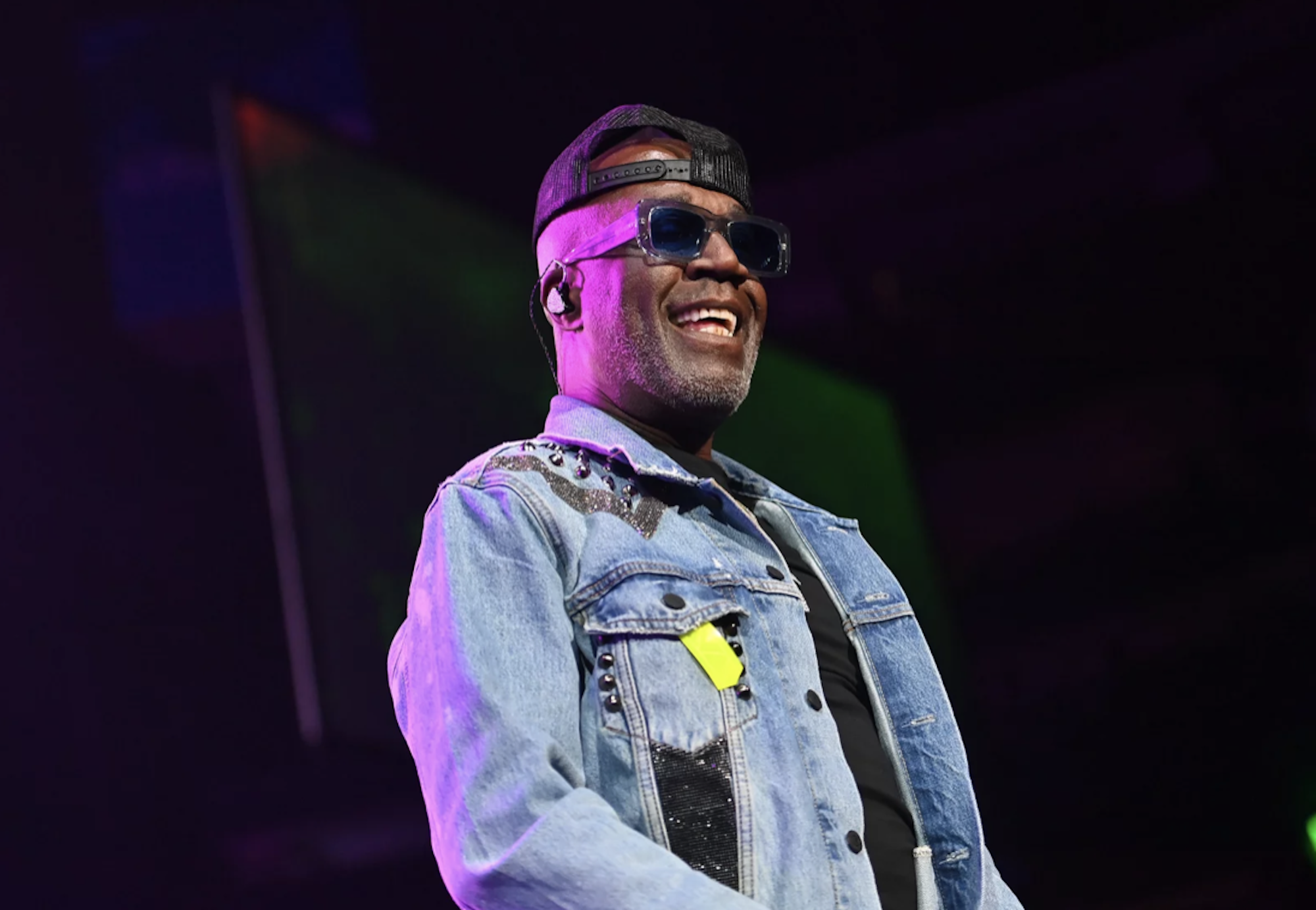 A Black man onstage wearing sunglasses and a denim jacket.