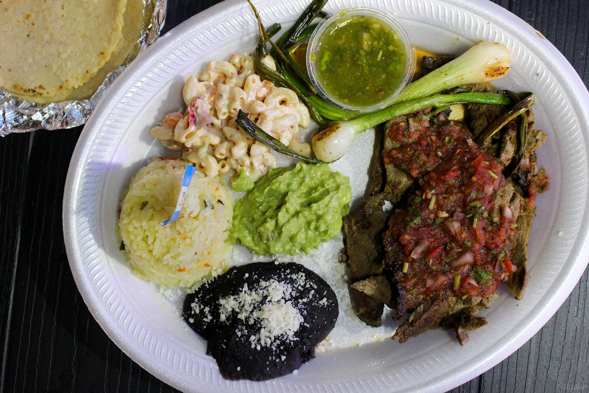 A Styrofoam plate with salsa-covered steak, rice, puréed beans and a side of tortillas.