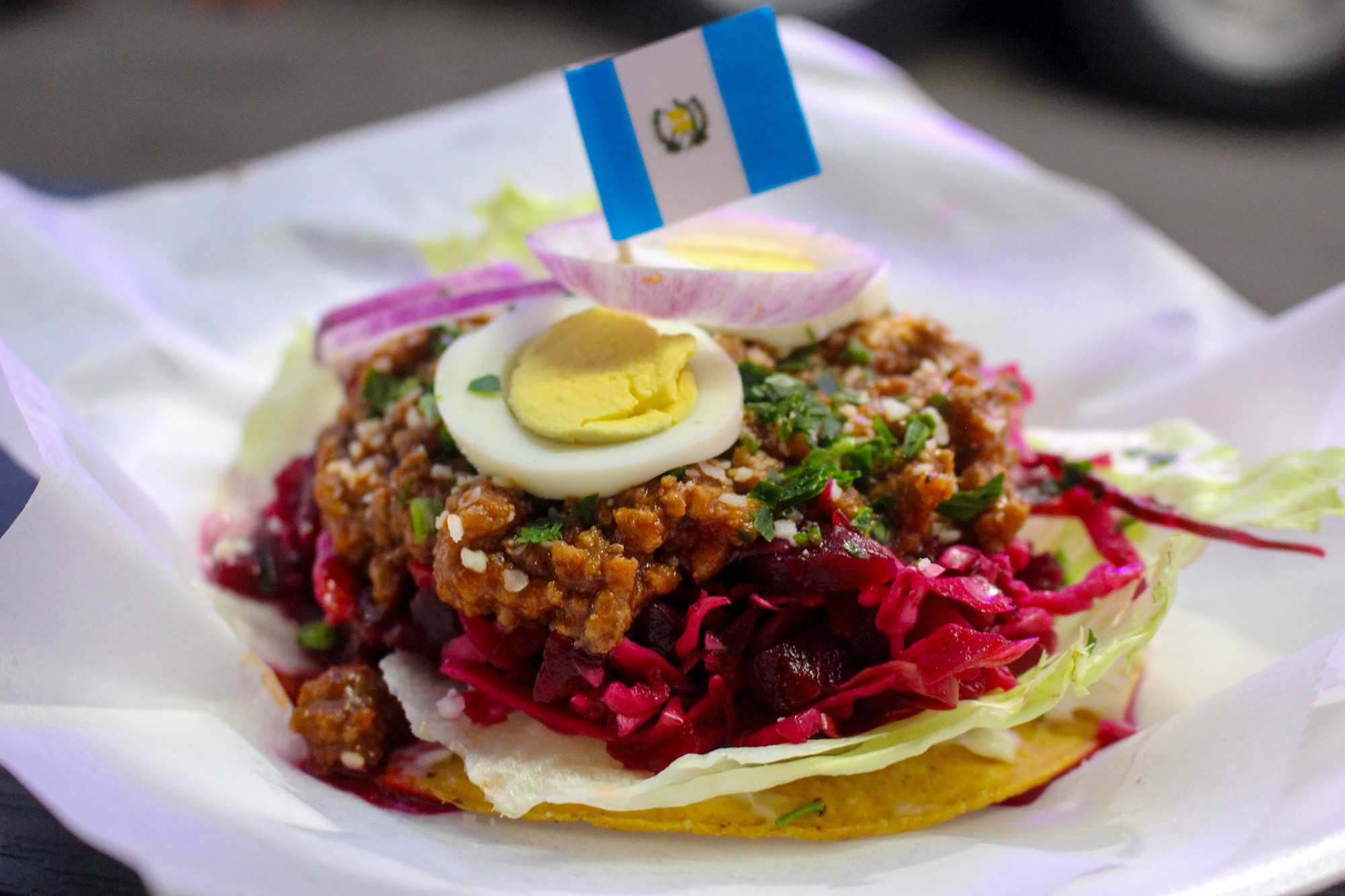 A tostada topped with ground beef, pickled beets and a slice of hard-boiled egg.