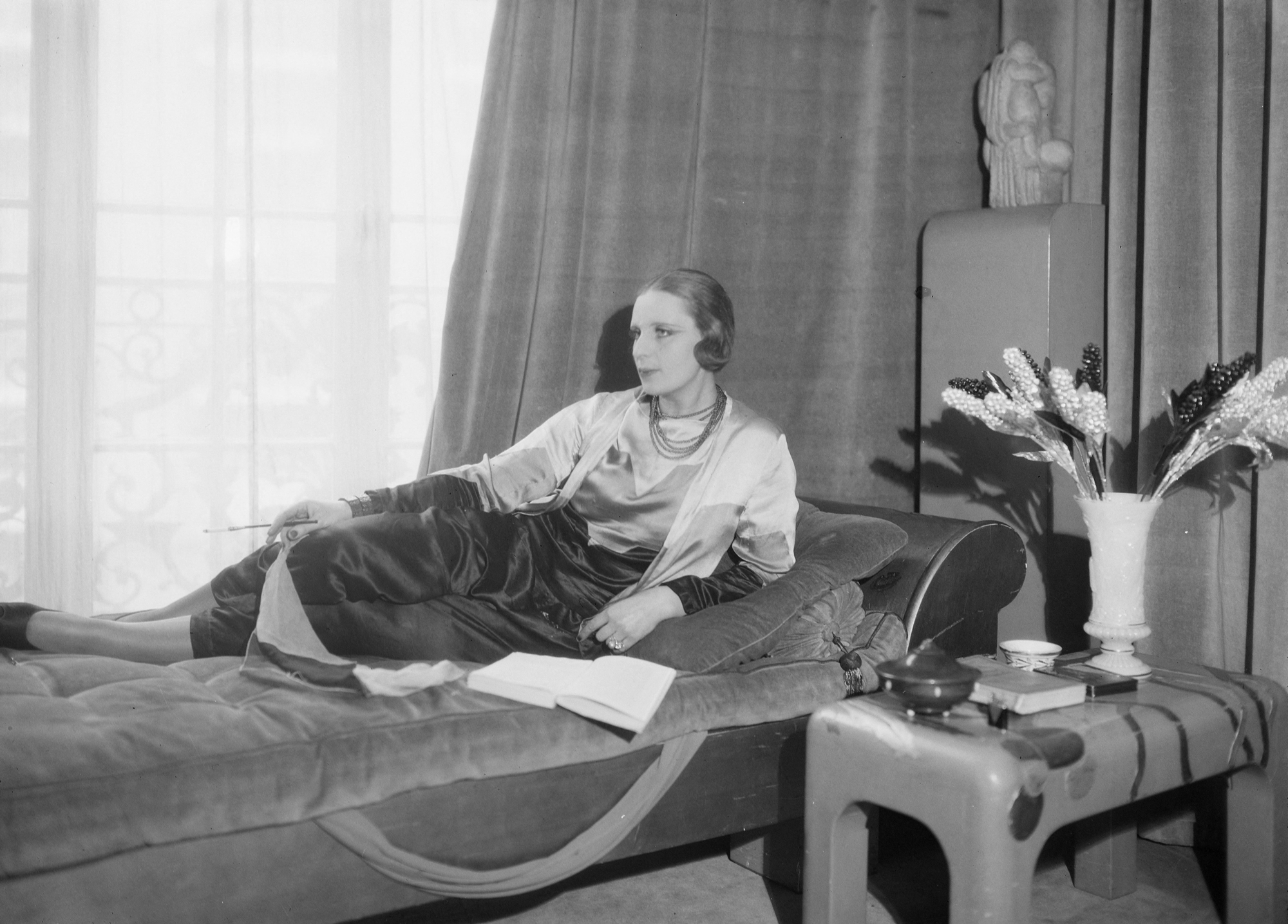 black and white photograph if a woman lounging on a daybed with a cigarette