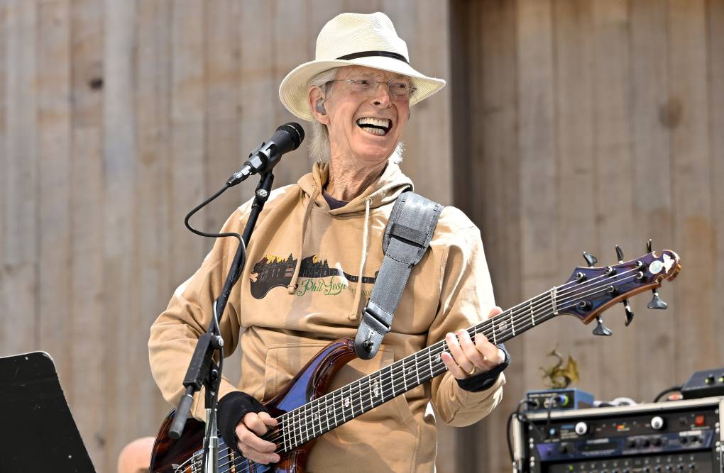 an older man plays bass on stage while smiling