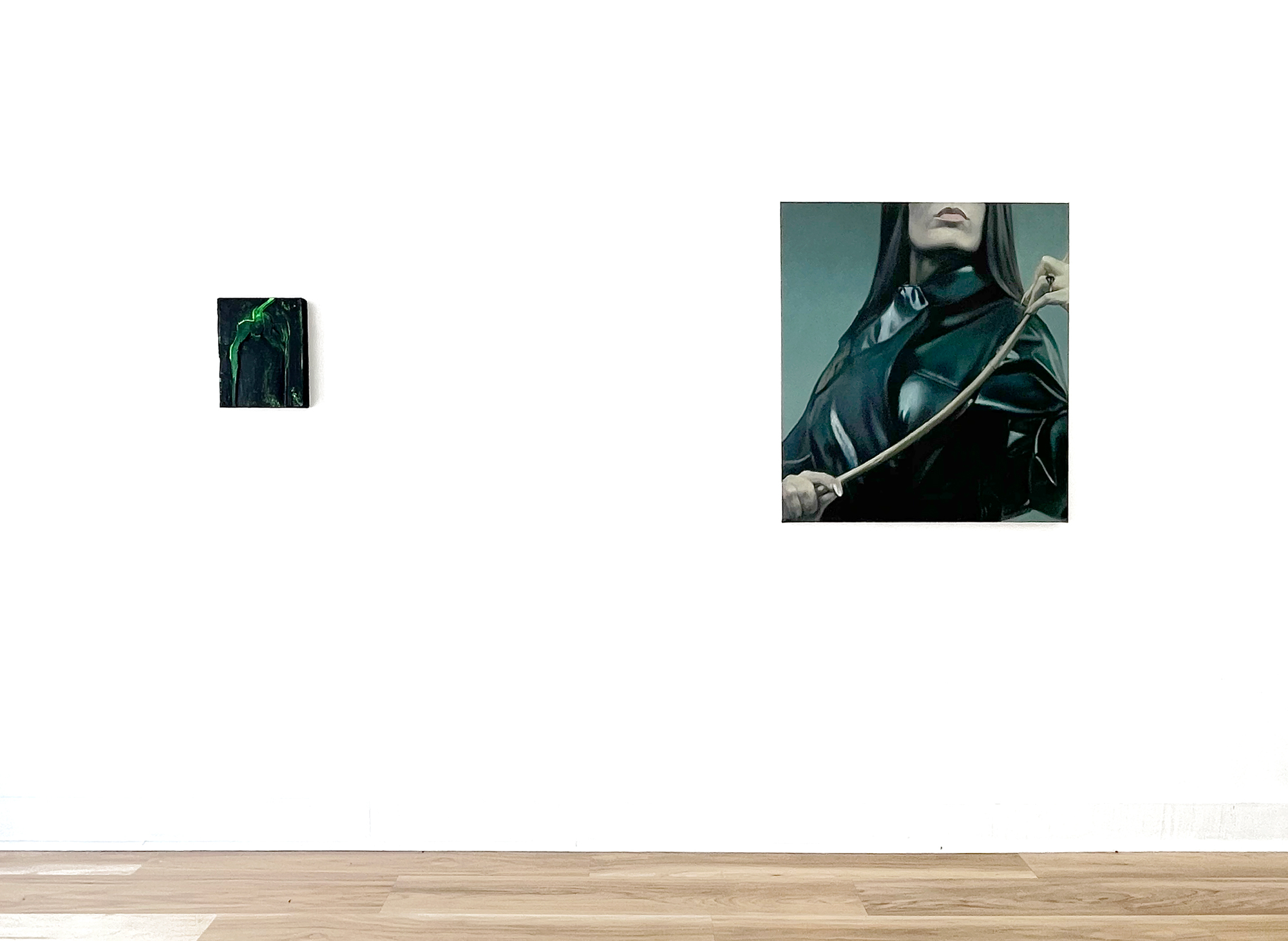 two paintings on white wall, one small and abstract, the other of a figure in leather holding a switch