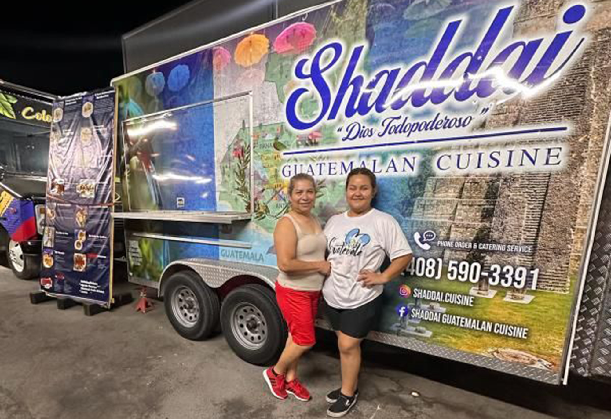 Two women — the operators of the Shaddai food truck — pose for a portrait in front of the truck.