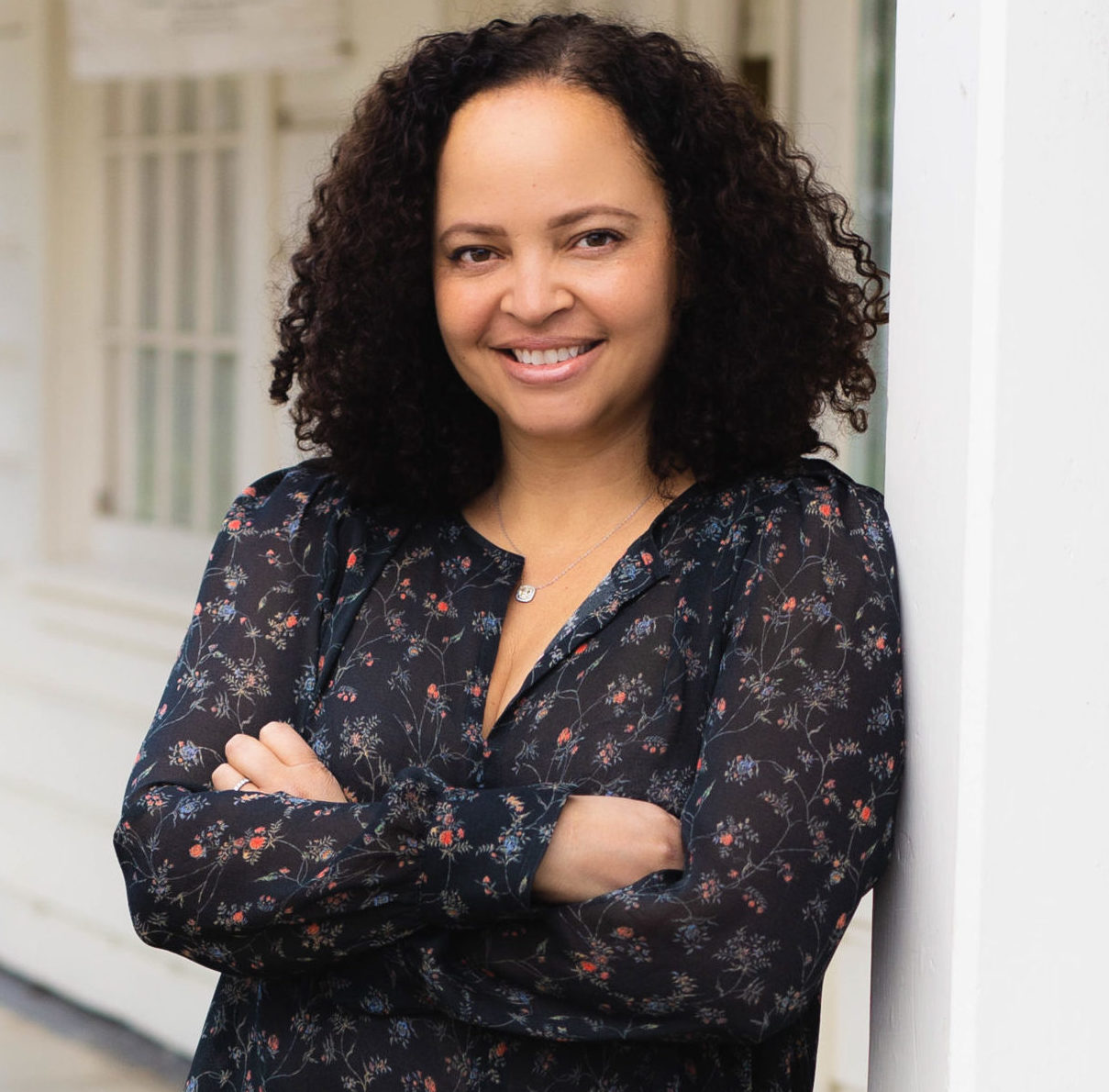 woman with shoulder length curly dark hair, arms crossed smiling