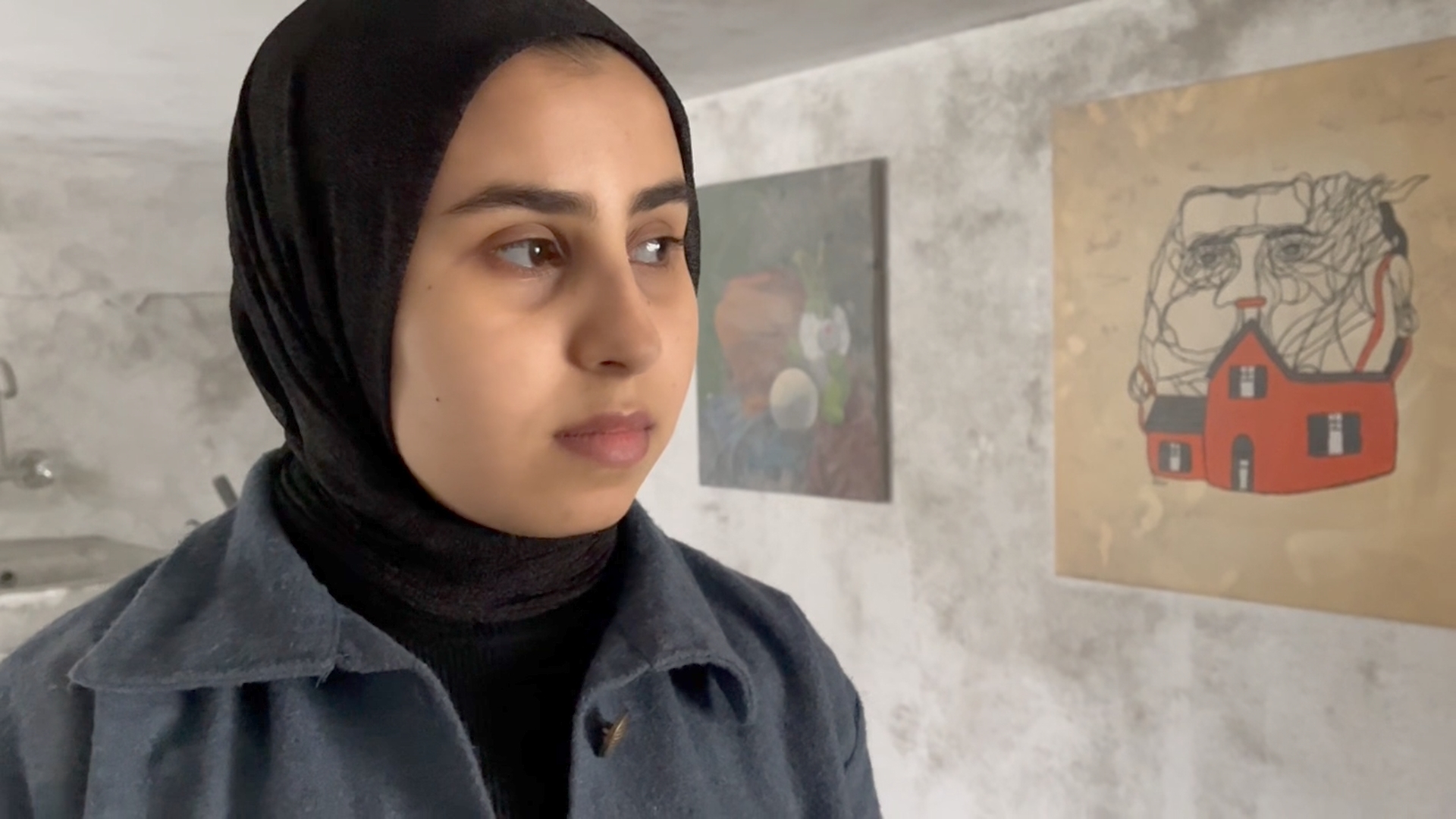 woman in hijab stands next to art prints hung on wall