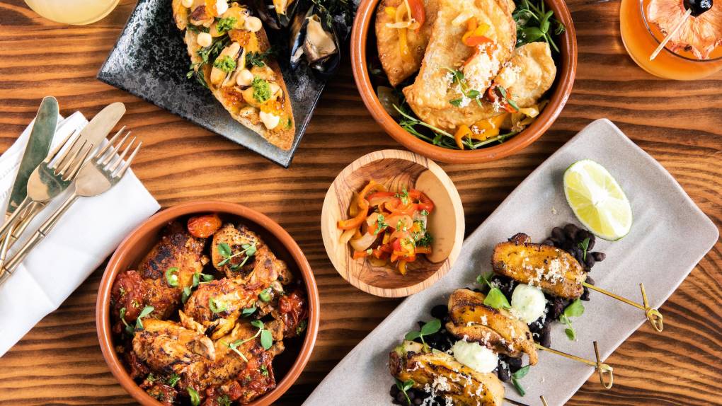 Overhead view of a spread of Afro-Latino small plates, including fried empanadas and chicken wings.