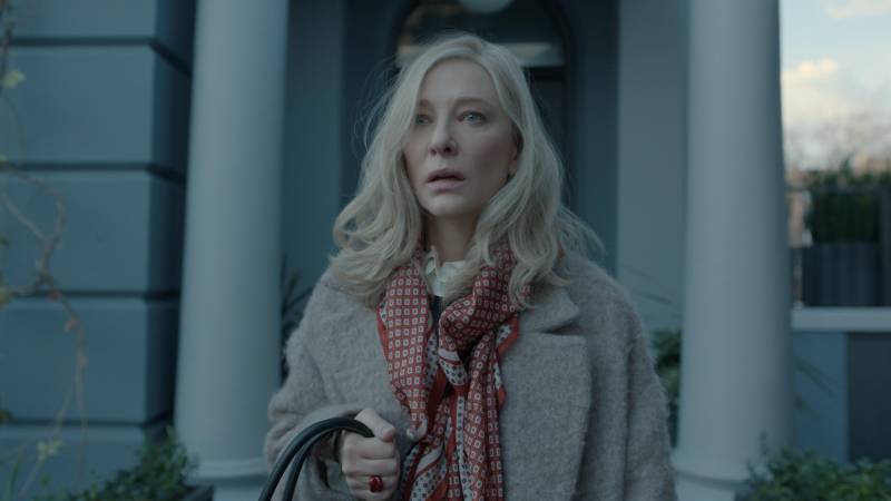 A blond white woman stands outside a front door, looking stunned.