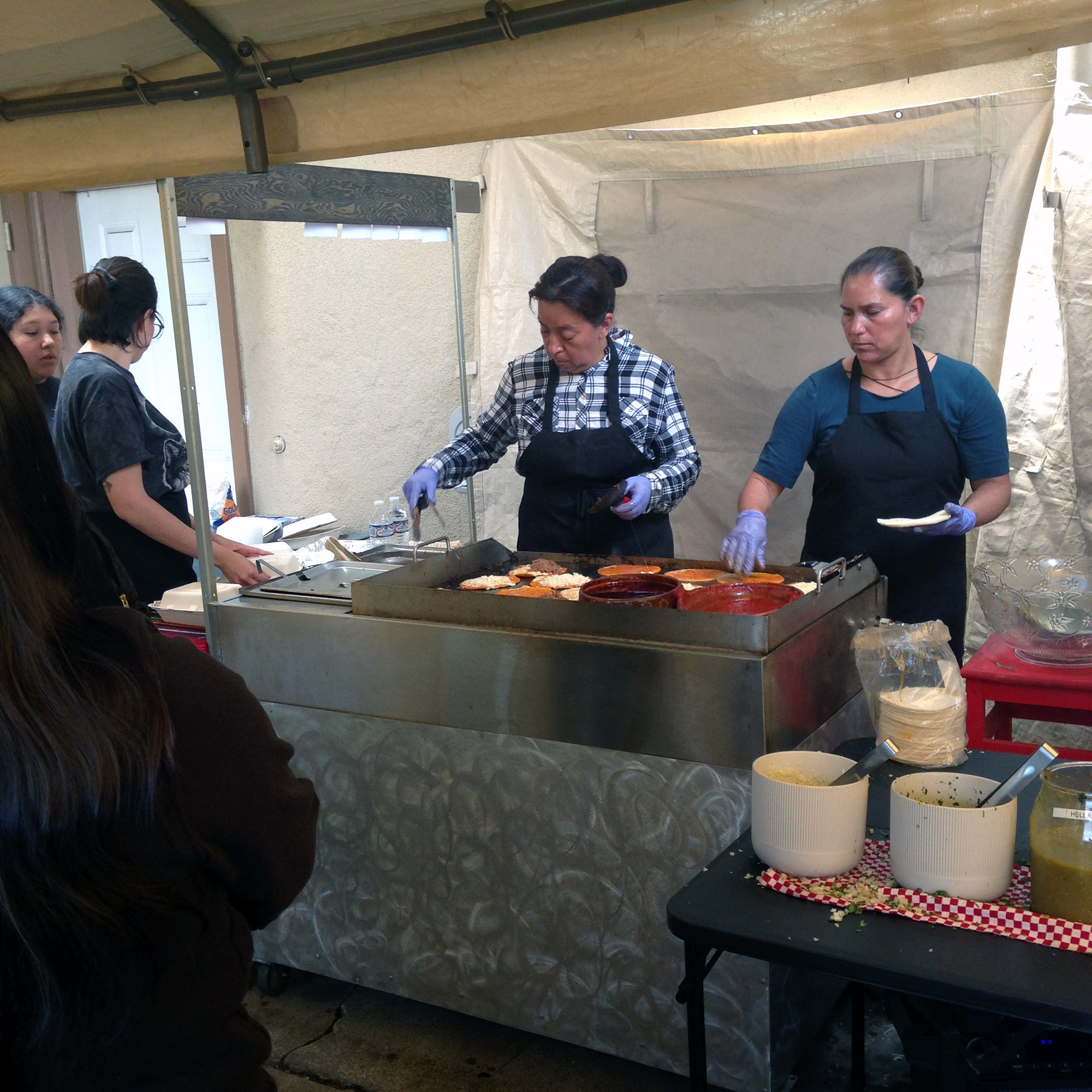 A cook makes tacos on a flat-top grill set up inside a tent.