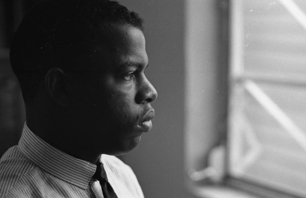 A young Black man wearing a shirt and tie looks out of a window, his face in profile.