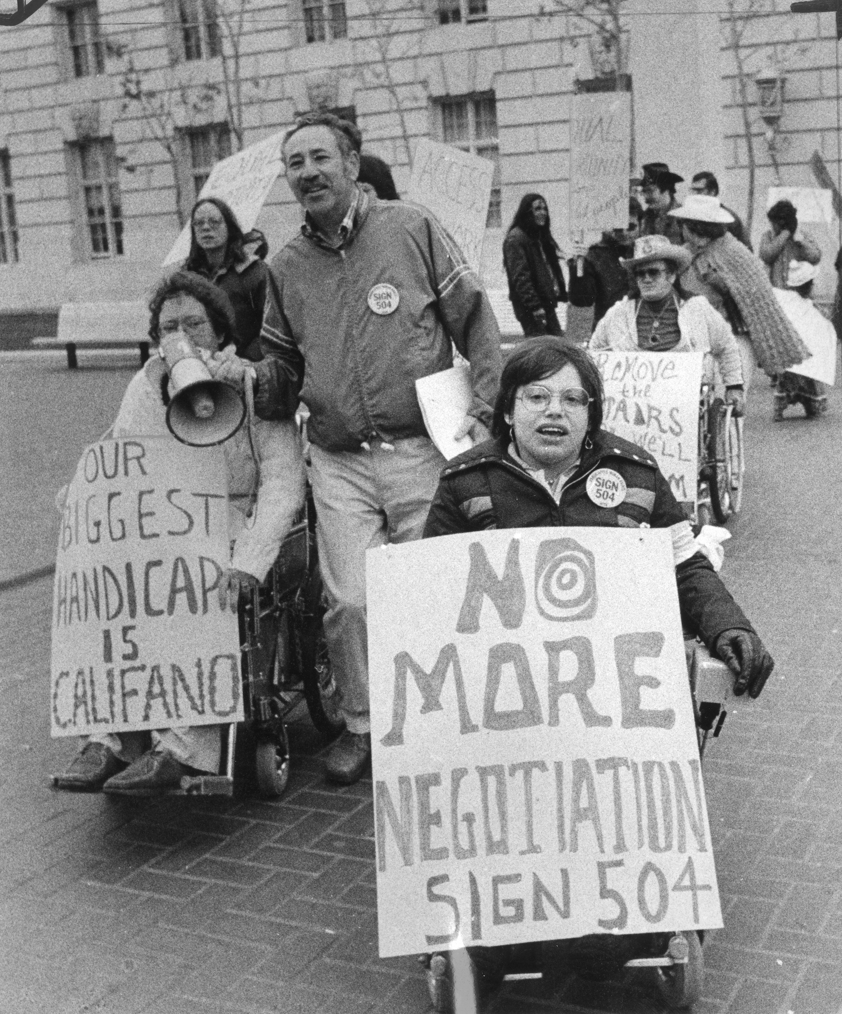 Men and women — some of them using wheelchairs — carry protest signs in the street.