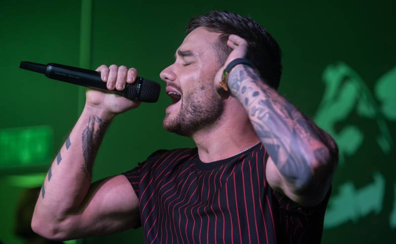 A young man with tattooed arms sings passionately on stage.