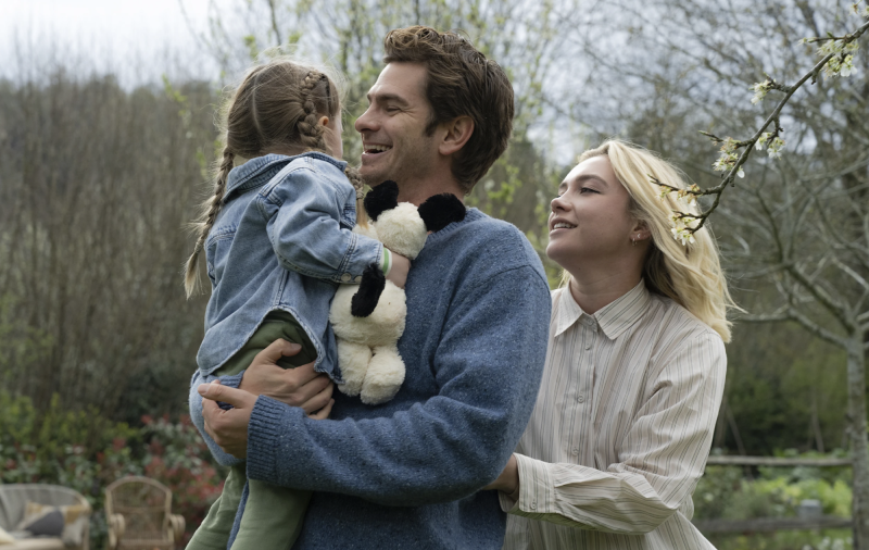 A man and woman in their mid-thirties smile at a child in the man's arms, during a wintry walk outside.