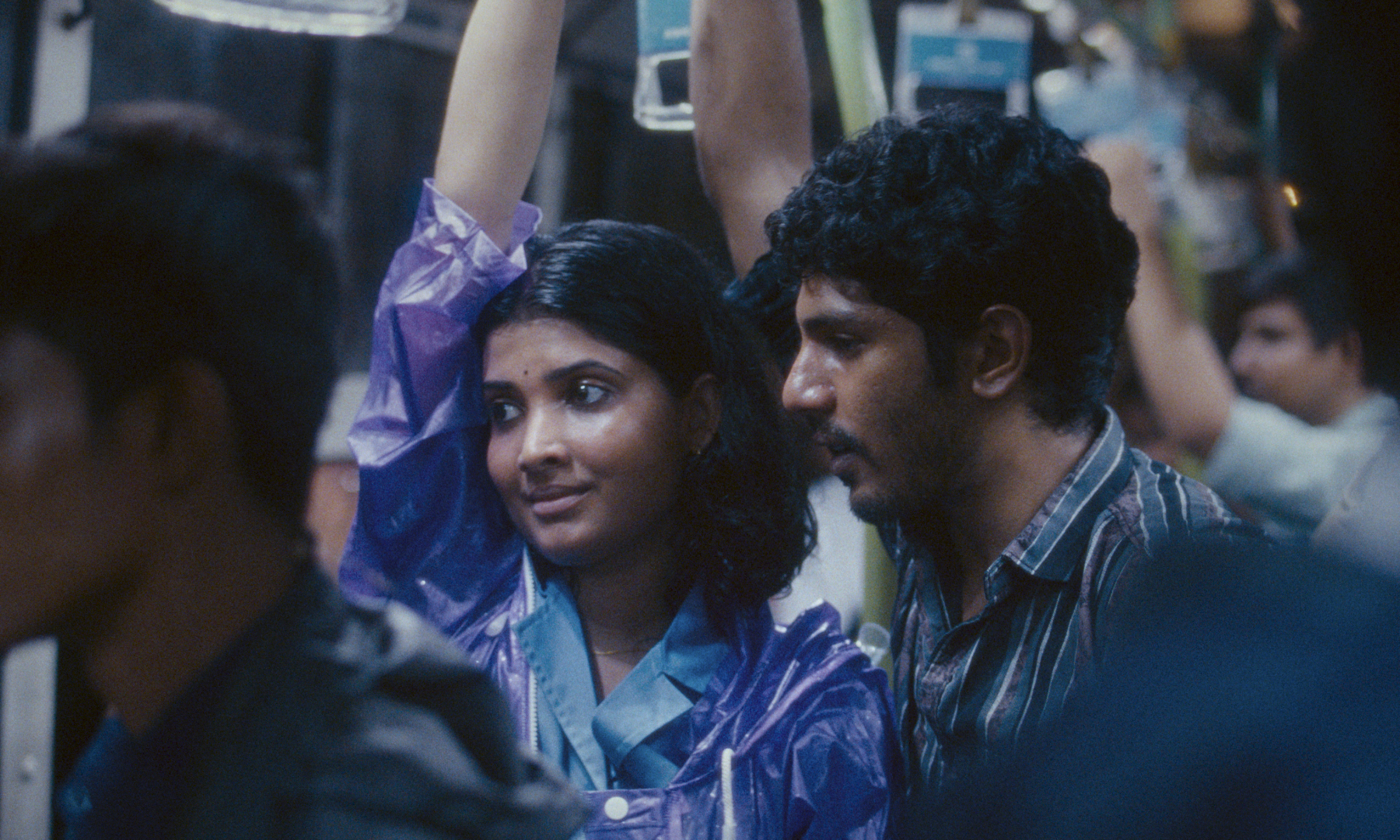 man and woman hold on to supports above their heads in crowded train 