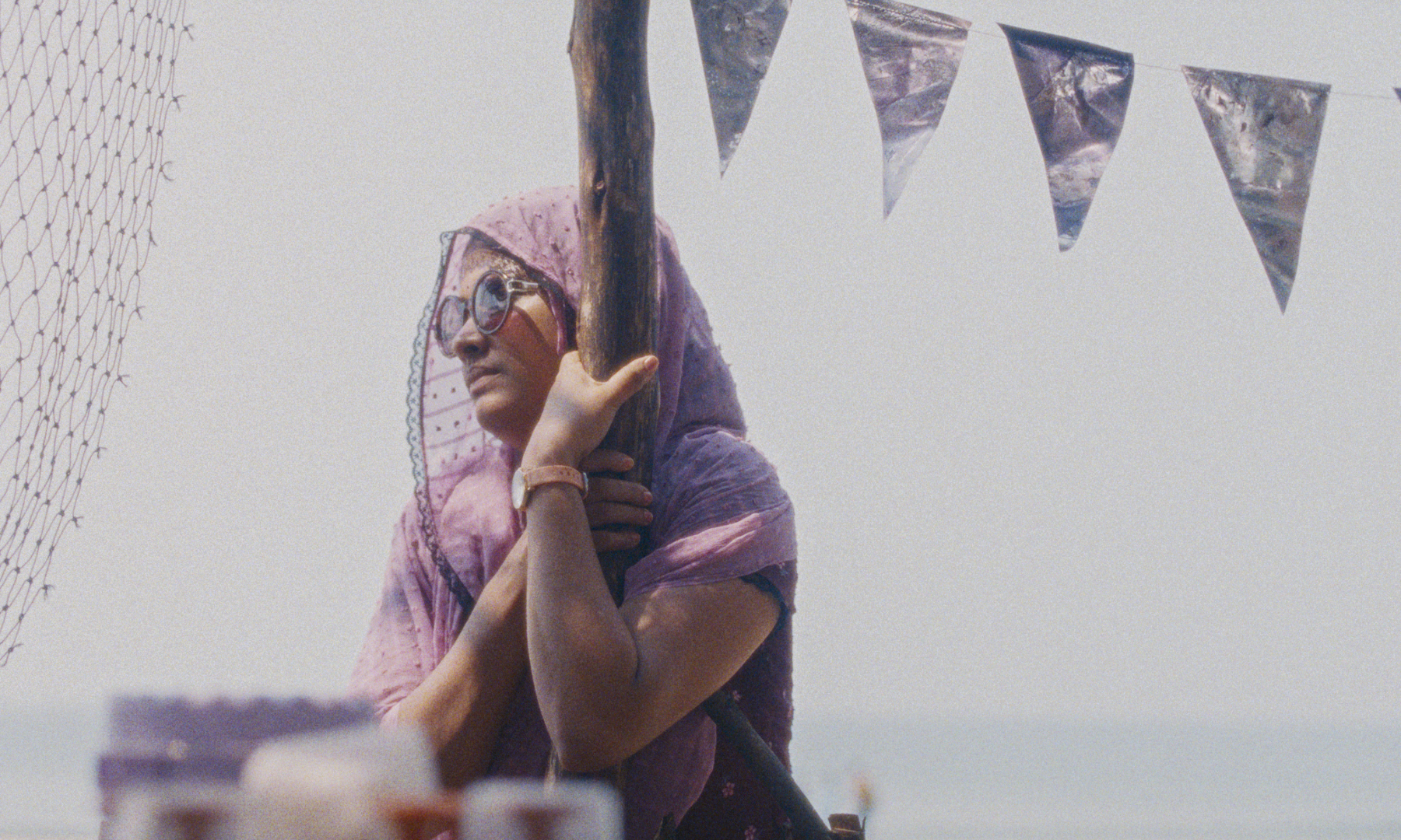 woman with headscarf and sunglasses holds onto post with flags