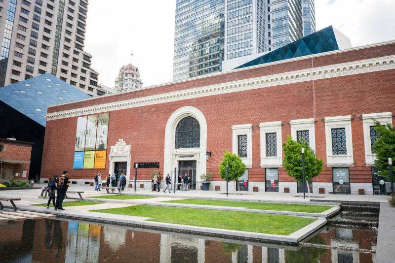 large brick building with angled additions facing plaza with lawn and water