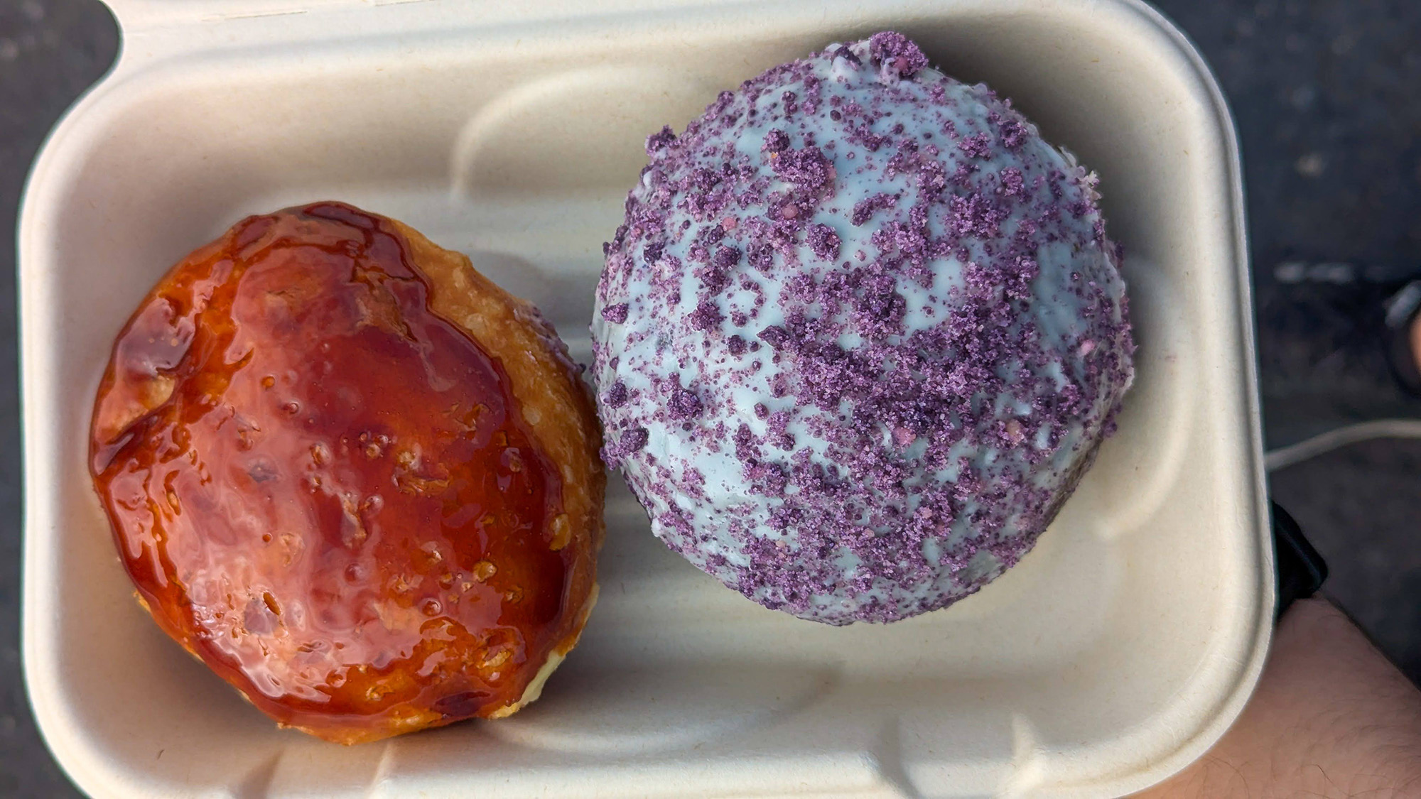 Overhead view of an ube doughnut and creme brulee doughnut in a takeout container.