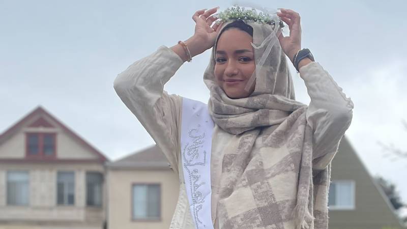 woman in hijab smiles, holding crown on head