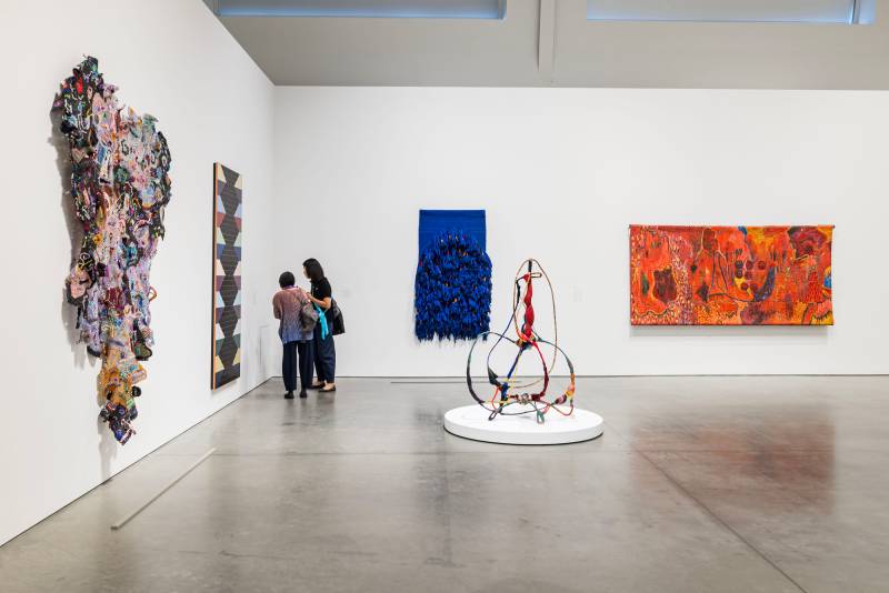 two people look closely at artwork on walls in gallery hung with colorful textile pieces