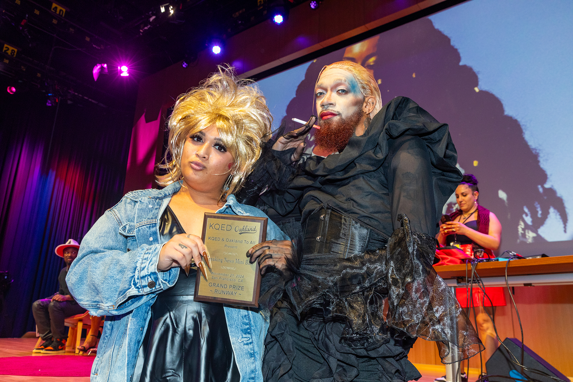 Two people stand in the middle of an auditorium and hold a plaque.