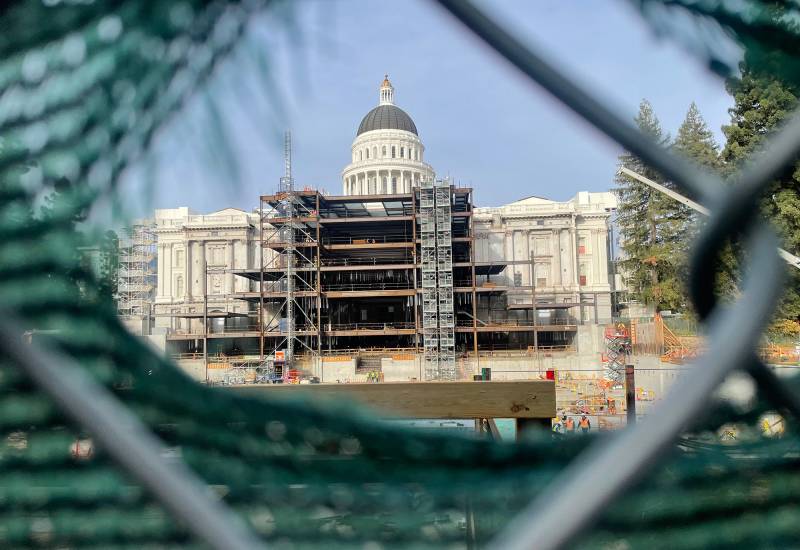 View of the California State Capitol building, under construction, as viewed through a chainlink fence.