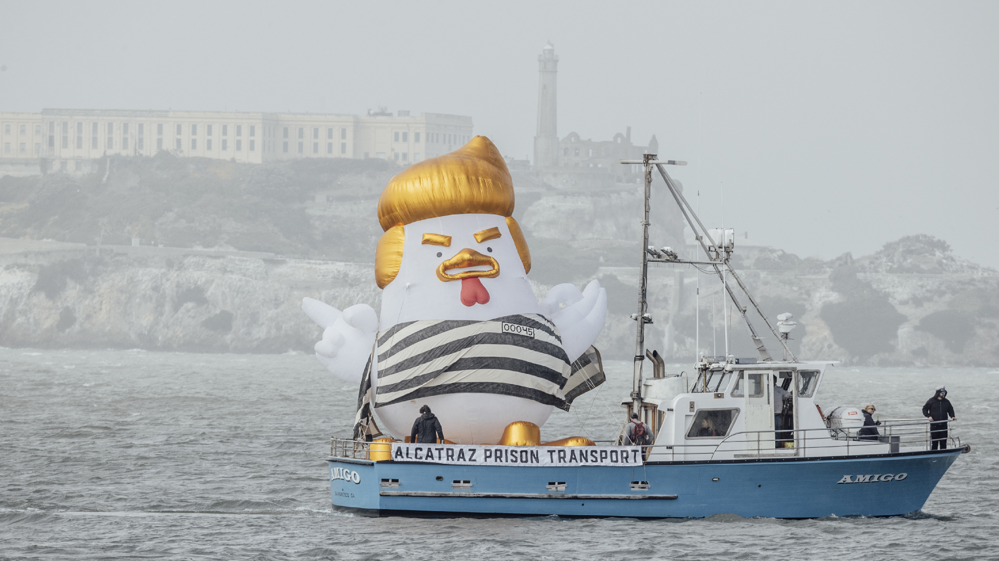 inflatable bird with yellow hair in prison stripes on boat labeled Alcatraz Prison Transport