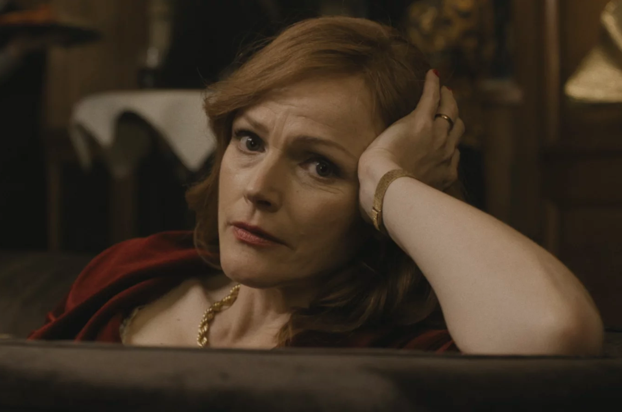 A red headed woman rests her head on her left hand while reclining on a couch. She looks concerned.