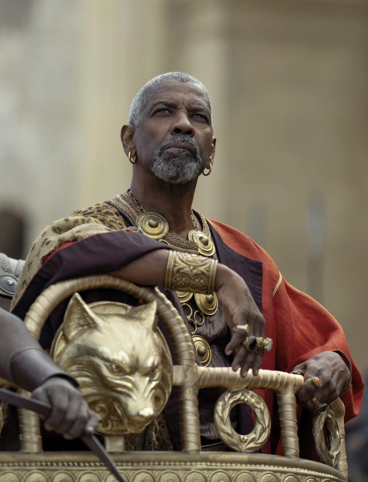 A Black man, regally dressed in old Roman attire sits within an elaborate gold balcony.