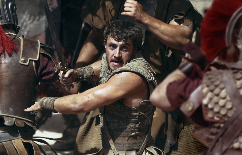 A gladiator swings a sword, surrounded on all sides by soldiers in armor and trojan helmets.