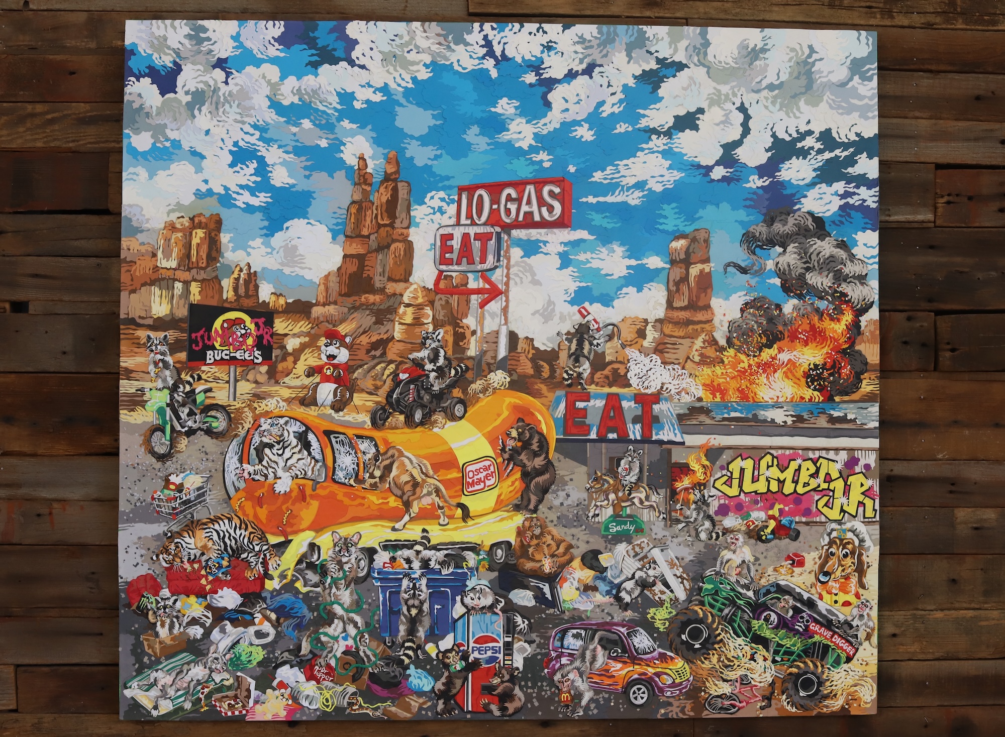 A paper collage artwork featuring desert landscapes, a fire outbreak and raccoons, monkeys, big cats and possums behaving debaucherously.