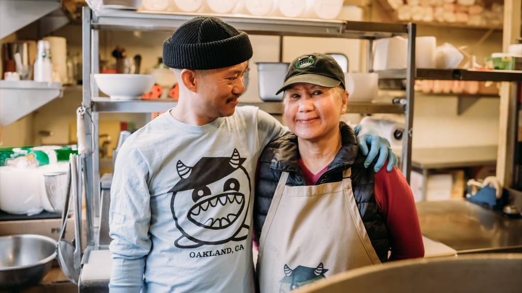 A mother and son pose for a portrait inside their restaurant kitchen.