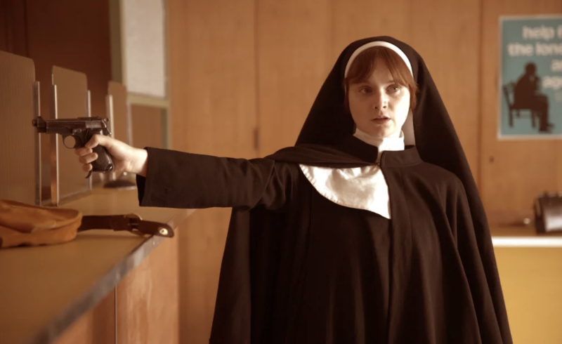 A white woman dressed as a nun points a gun at a bank teller's window.