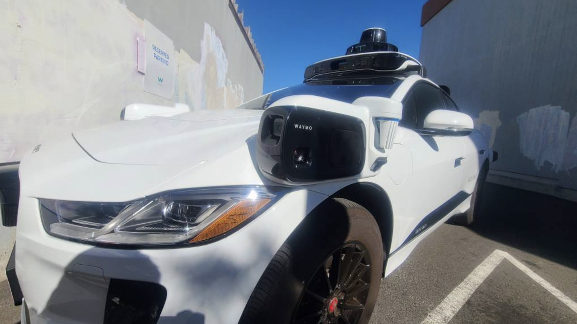 A Waymo autonomous car photographed between two walls using a fisheye lens.