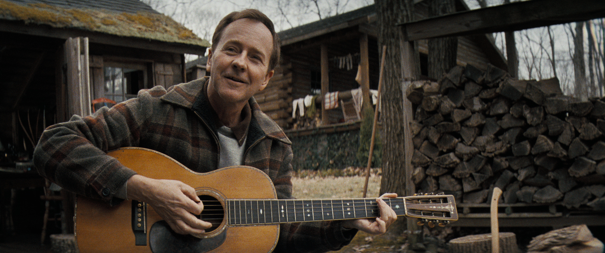 man holds guitar outside stone house