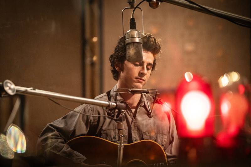 man sits in recording booth with guitar, mic hovers above