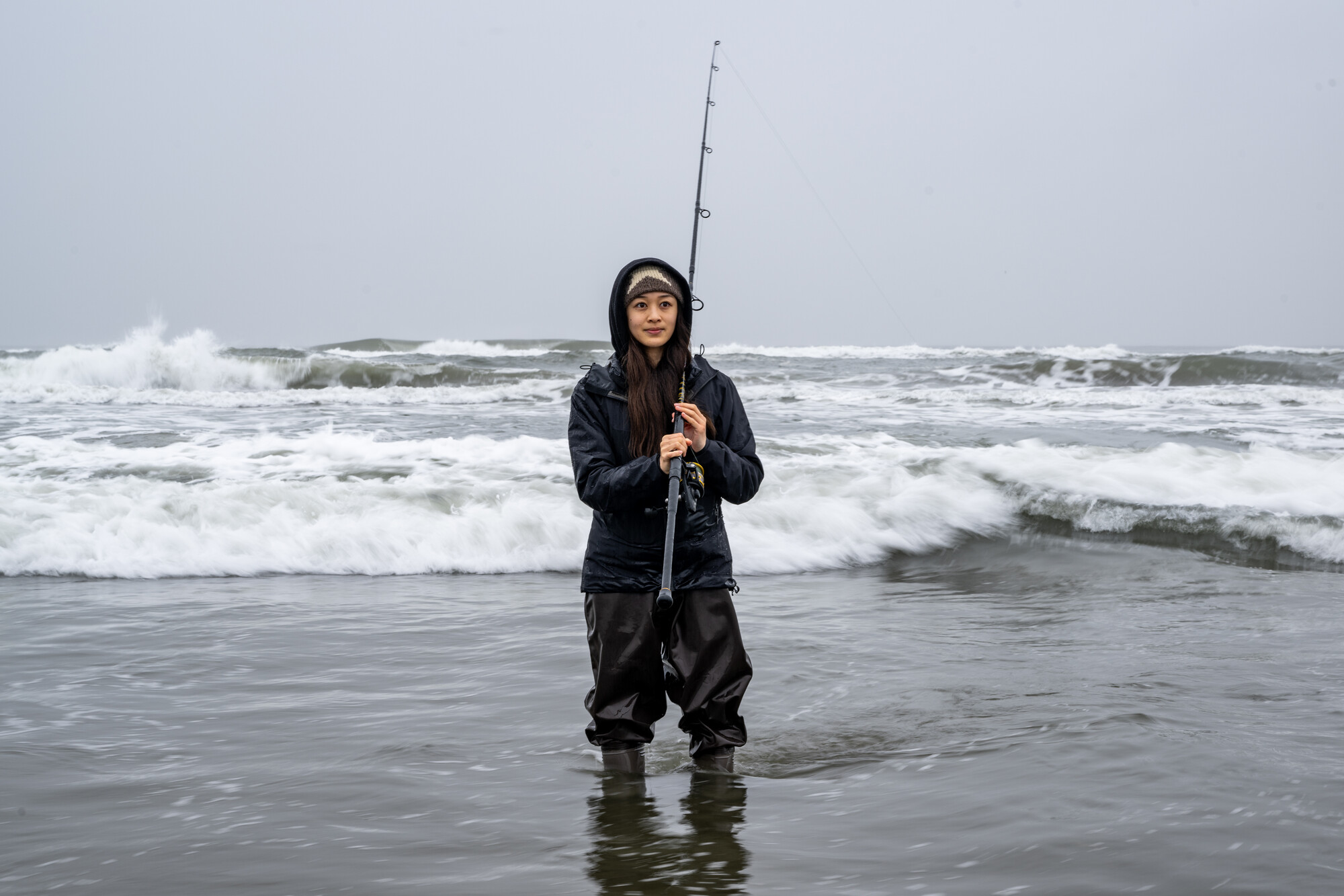 A fisherman holds her fishing pole as she walks back in from the edge of the water.