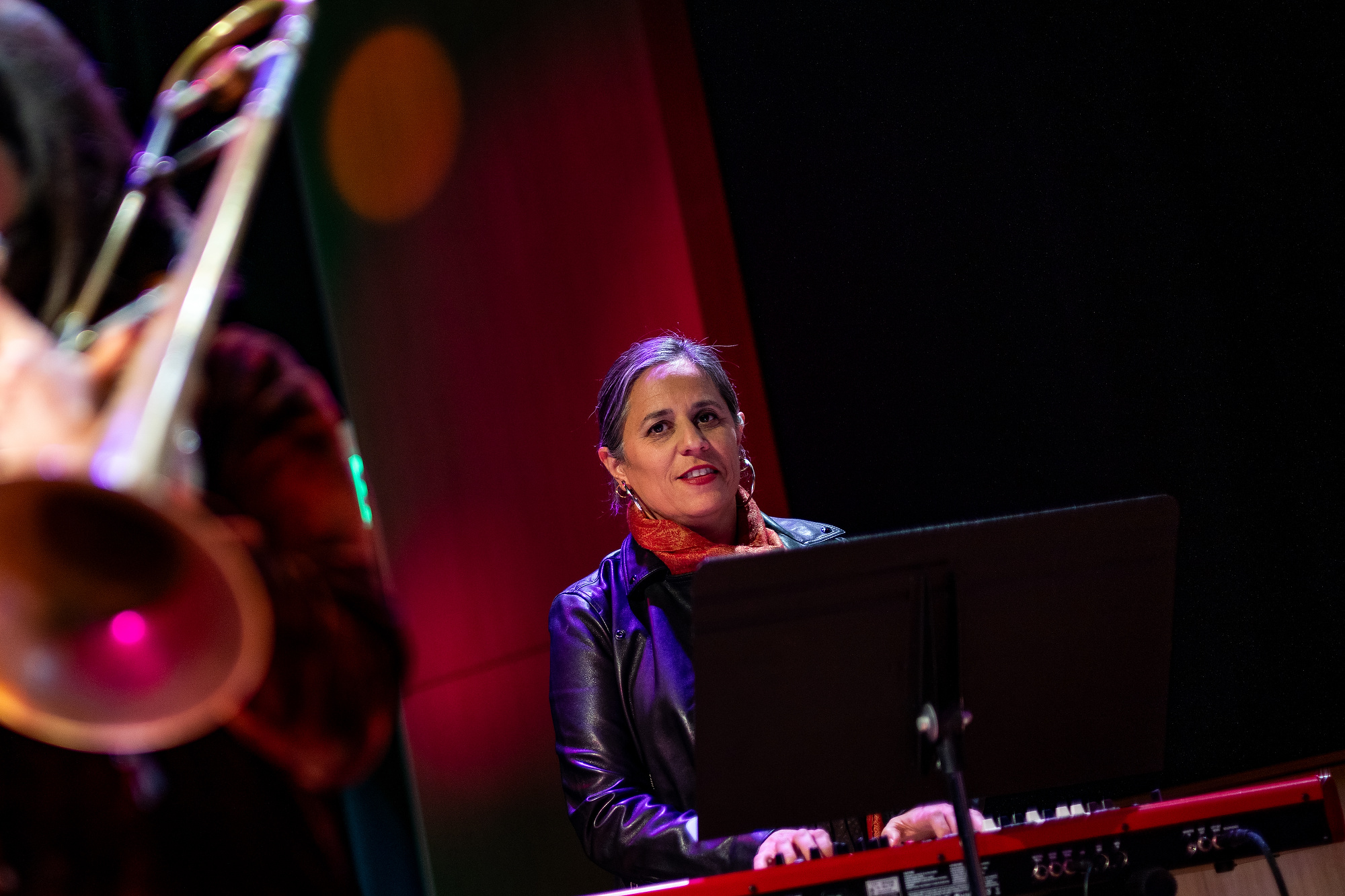 a woman in a black leather jacket plays the keyboard