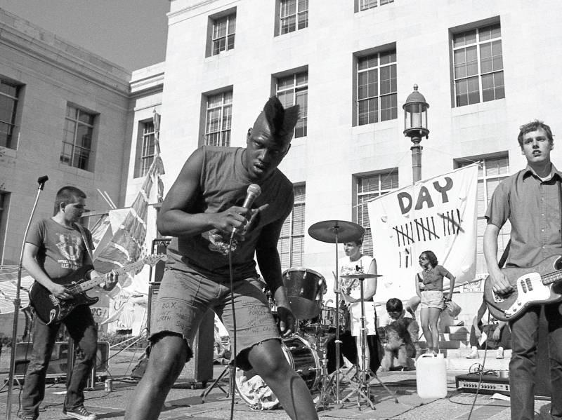 Punk band Special Forces plays at UC Berkeley's Sproul Plaza. Orlando, a tall Black man with a mohawk, stands in front with a microphone.