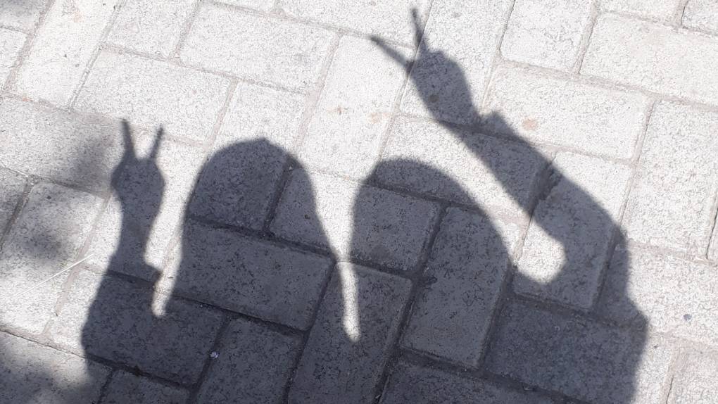 shadows of two people making peace signs on paved ground