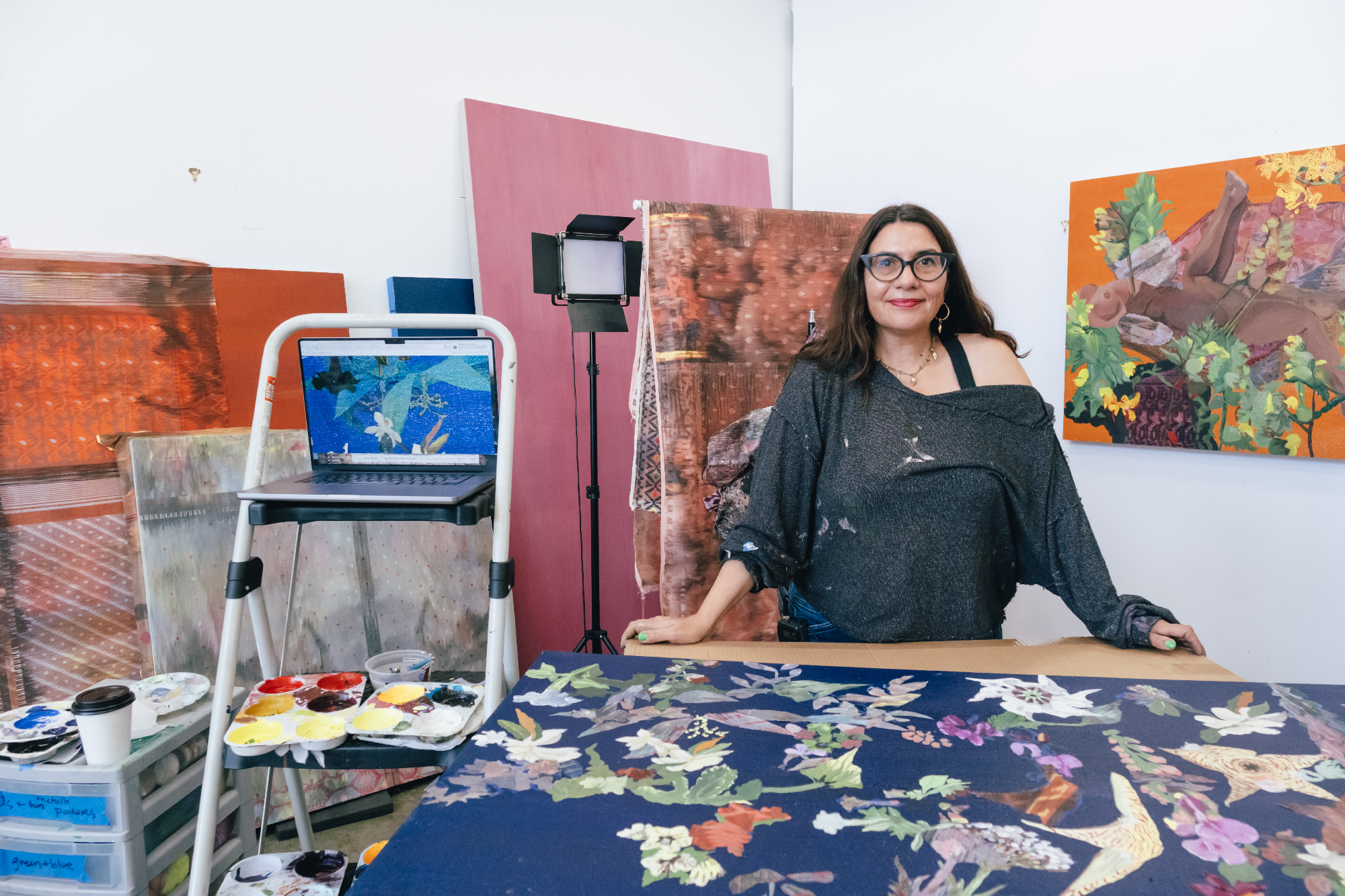 woman stands smiling among work table and large paintings