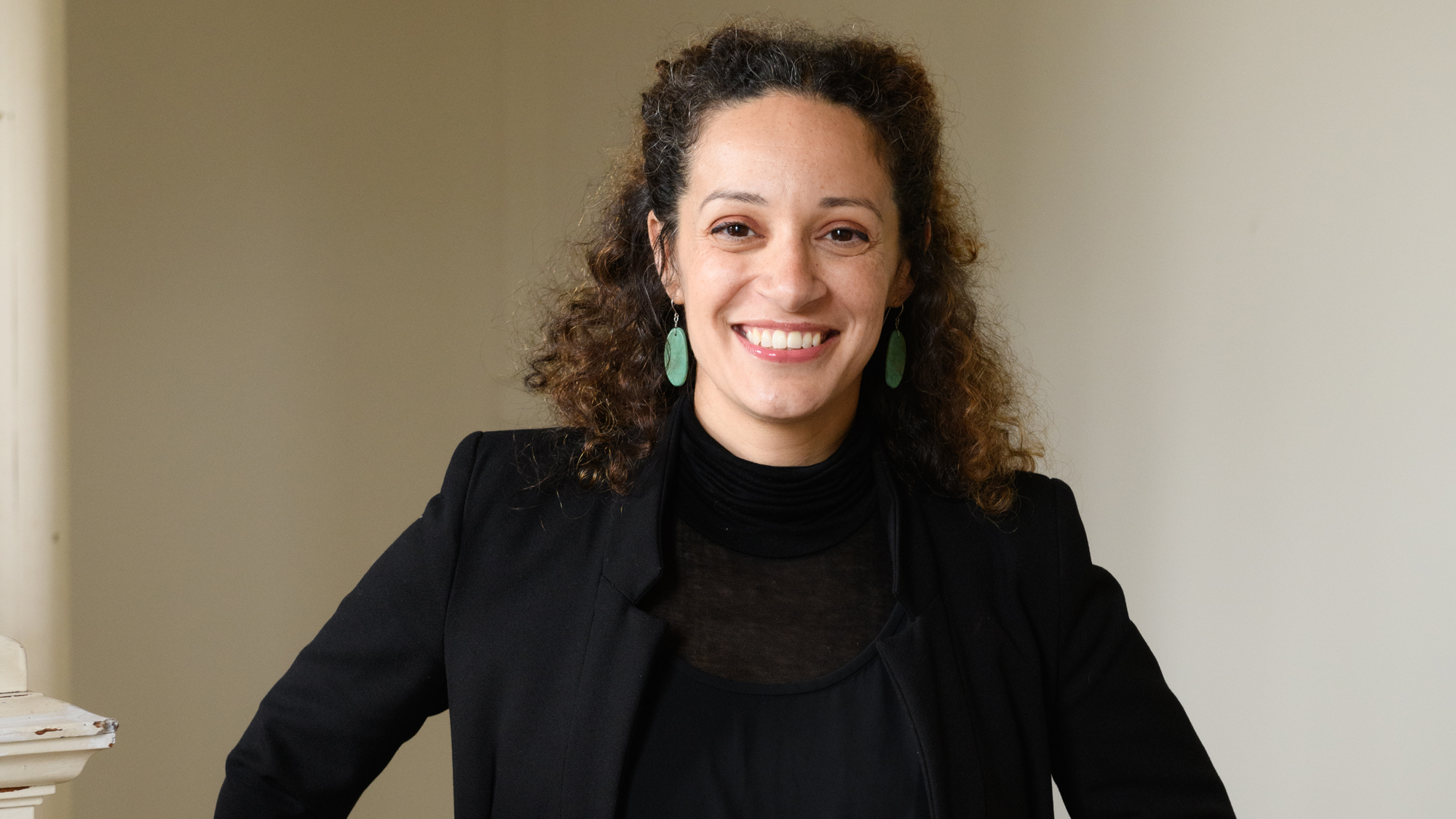 woman smiles in black outfit, shoulder-length curly brown hair