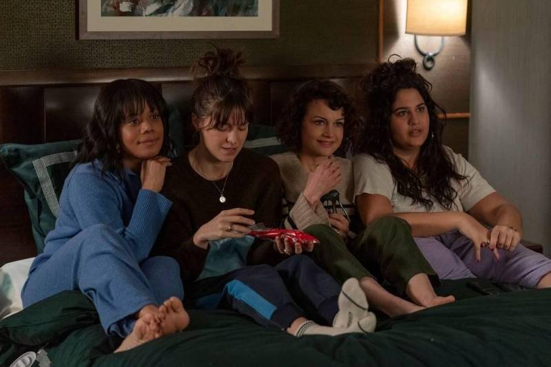 four young women sit on bed together