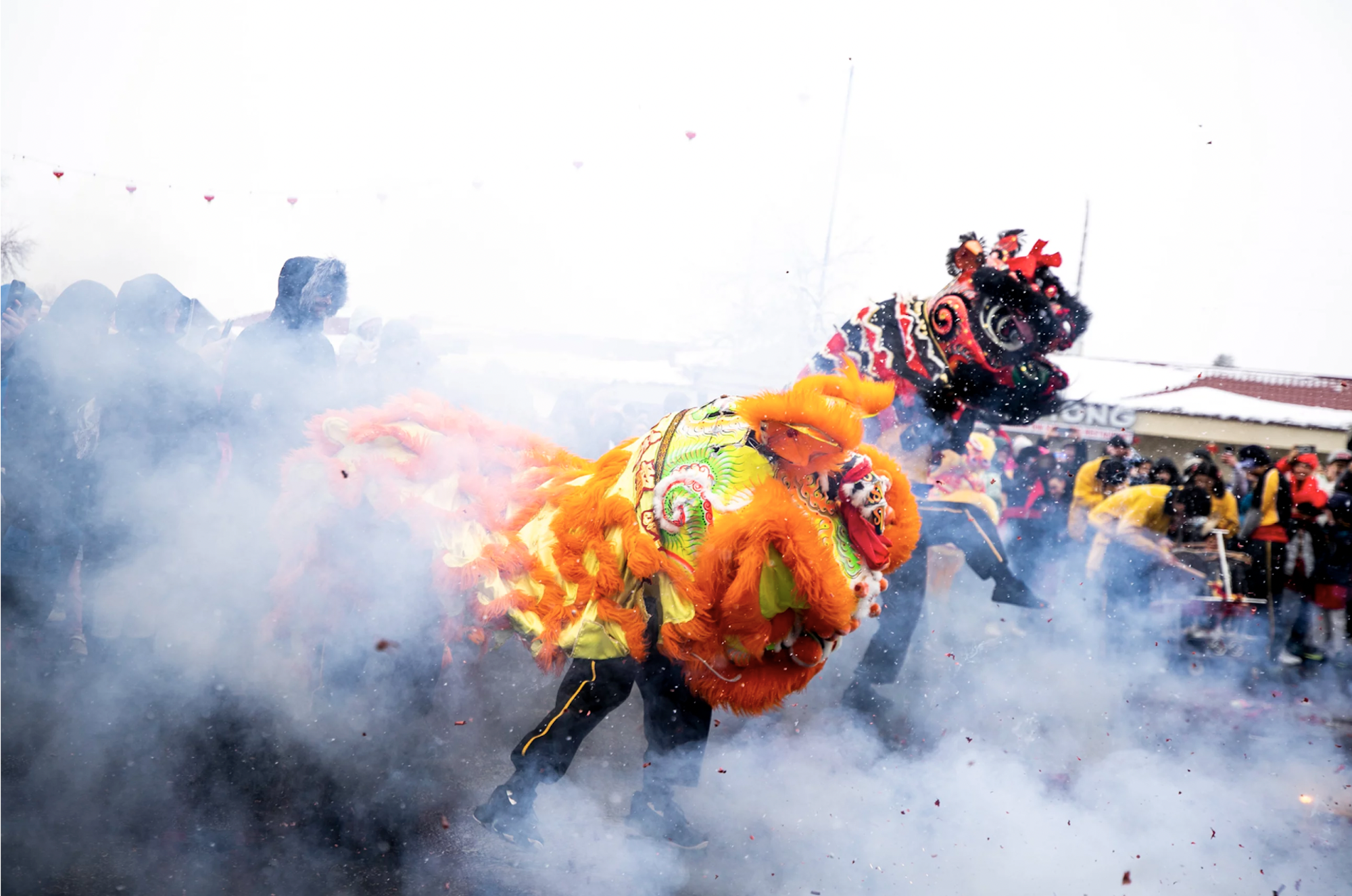 People wearing a colorful Chinese dragon costume dance through smoky streets during a daytime parade.