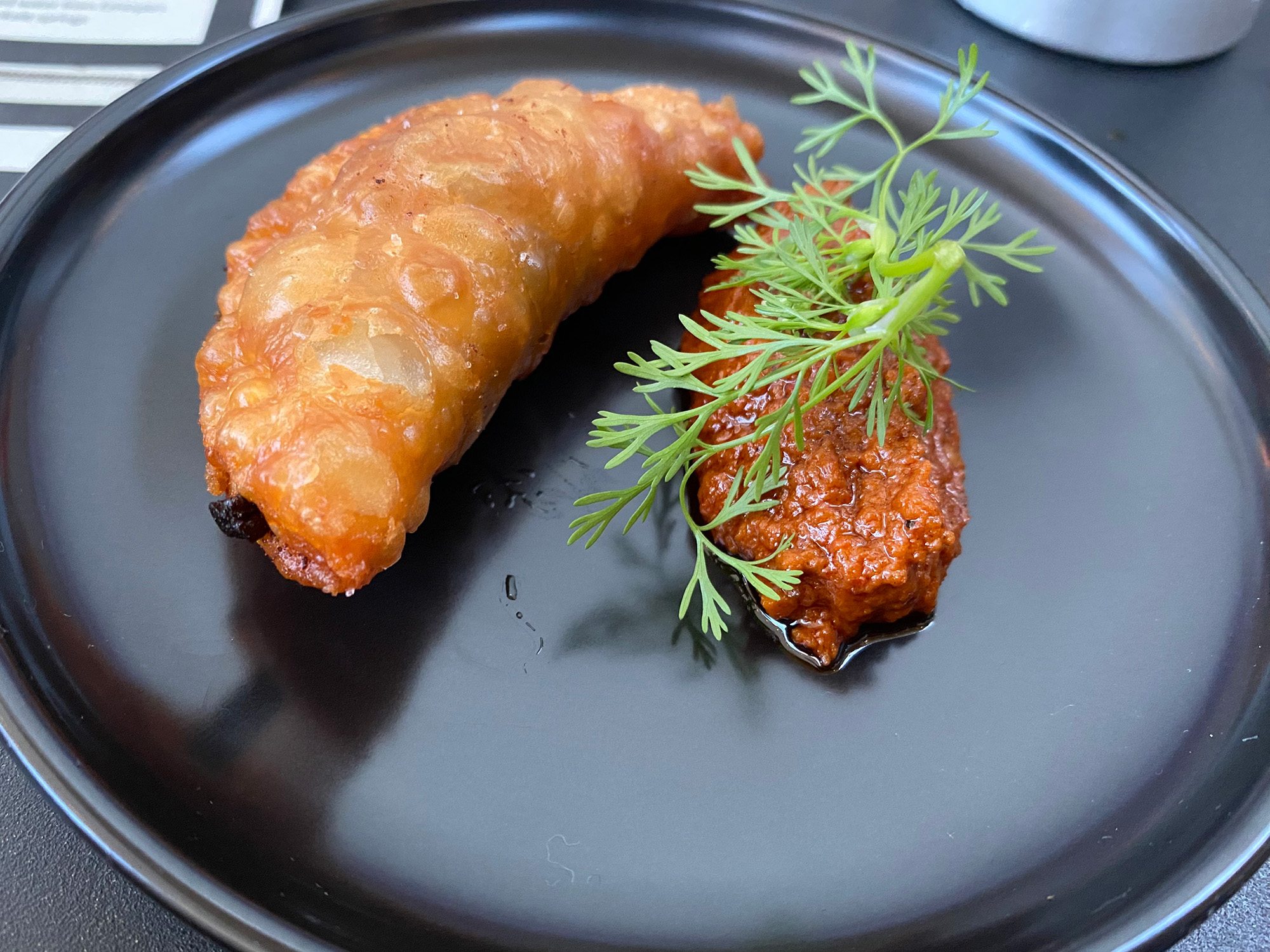 A fried meat pie, plated elegantly next to a sprig of green herbs.