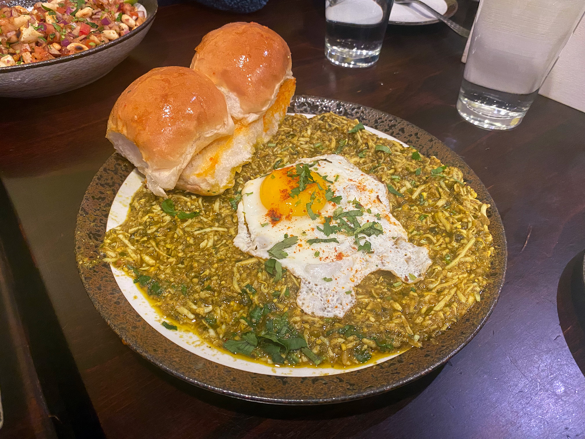 A large platter topped with grated hard-boiled eggs in green sauce, a fried egg, and two rolls.