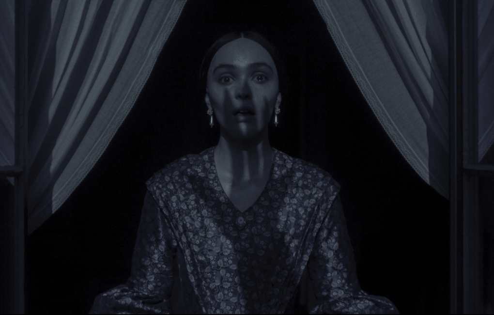 A woman in period clothing stands between curtains in a darkened window, the shadow of a clawed hand falling down her face.