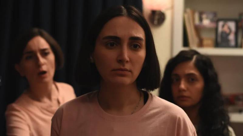 Three women of middle eastern descent, and of different ages, stand close together in a room, looking concerned.