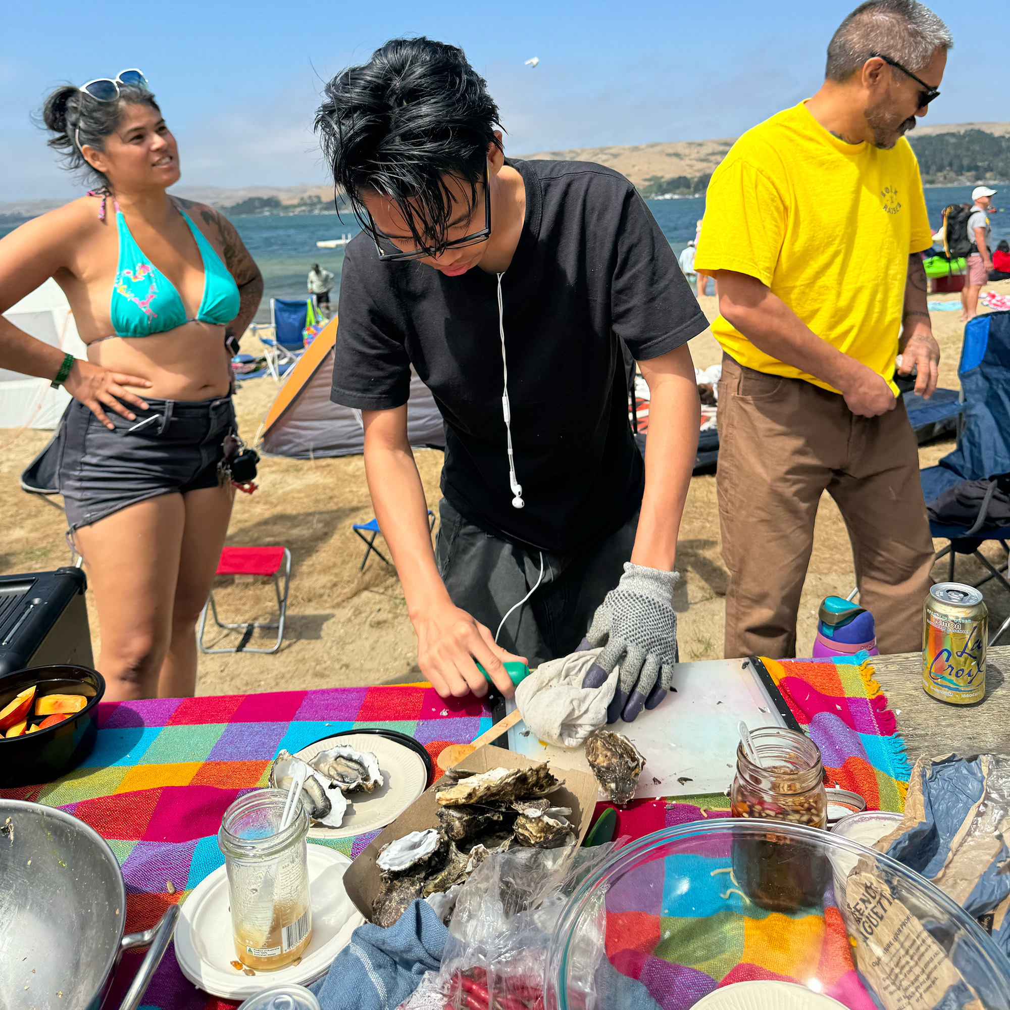 A young man leans over a picnic table as he shucks oysters.