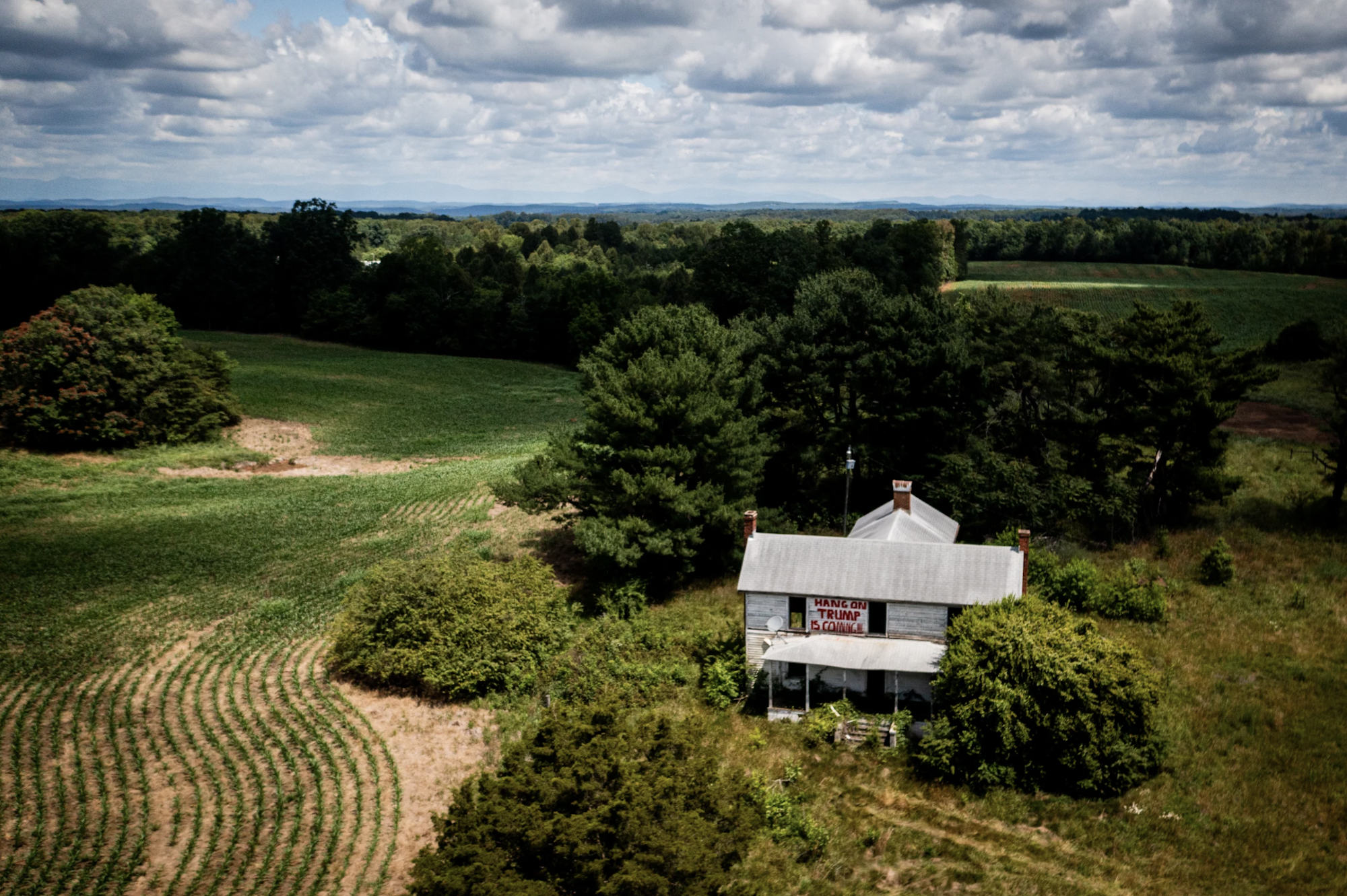 A large white house stands alone in an expanse of green fields and trees.